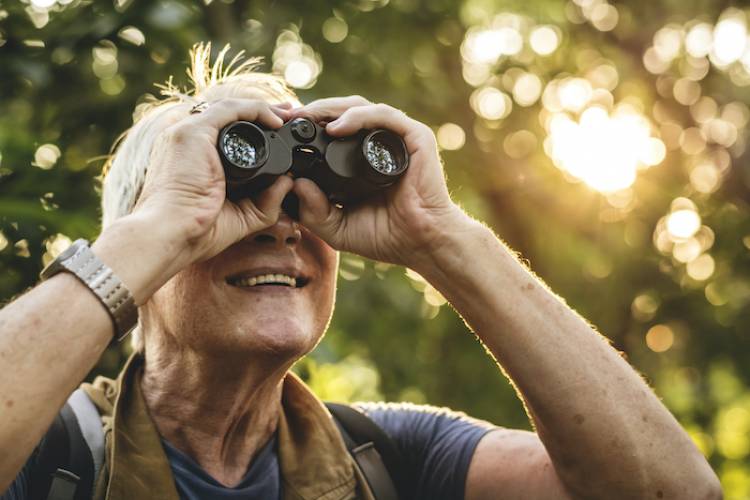 older woman with binoculars looking birdwatching in the forest