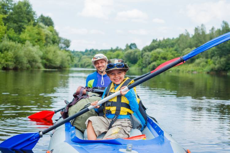 young kid and dad on a tandem kayak that is blue with blue and red ores on a river