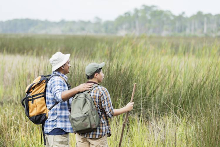 man and son hiking through the grasslands with sun hats on