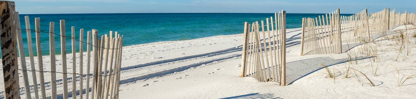 gulf shores beach alabama with fence in foreground and bright blue sky