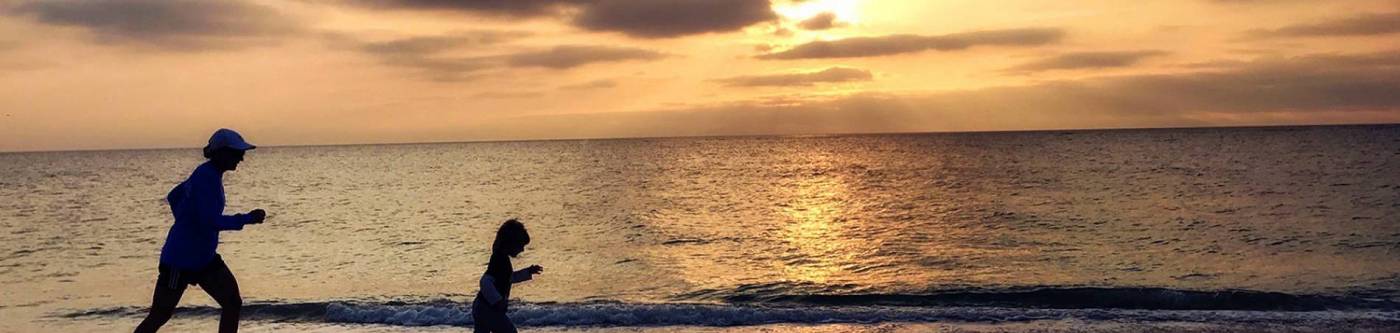 kid and parent running on beach as the sun sets