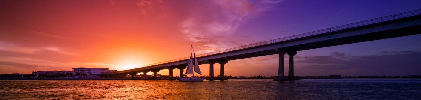 sunset along Orange Beach with a bridge in the foreground and bright blue, purple and red colors fill the sky